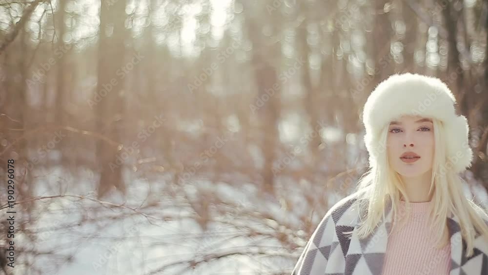 Beautiful young blonde girl with a warm blanket on her shoulders in the winter forest, looking into the camera Beautiful young blonde girl with a warm blanket on her shoulders in the winter forest, looking into the camera