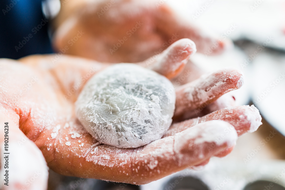 Fototapeta premium Hands shaping piece of mochi sticky glutinous rice cake dusted with starch flour to make dessert