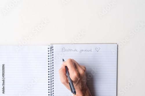 Фотография Directly above view of woman's hands holding black pen above spiral notebook gratitude journal on white table