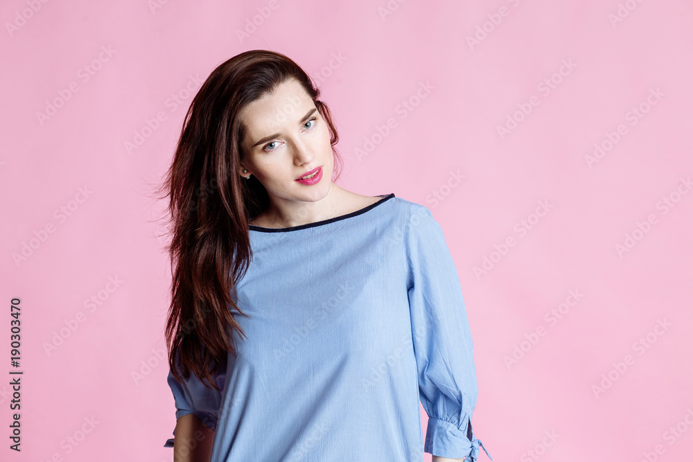 Portrait of a smiling cute woman brunette with long beautiful hair on a pink background. The girl in a blue dress looking at camera. Portrait of a smiling cute woman brunette with long beautiful hair on a pink background. The girl in a blue dress looking at camera.