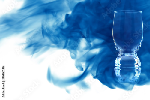 An empty glass of water enveloped in blue smoke.