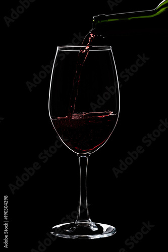 A large glass of red wine is pouring wine from a bottle of red .