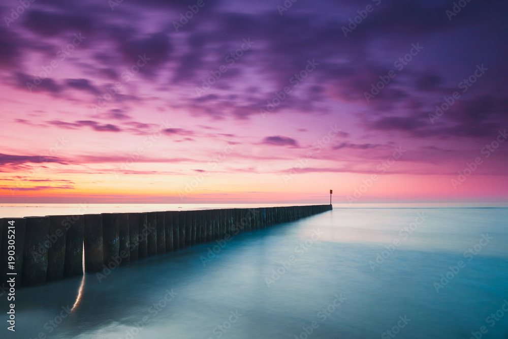 Sunset on the beach with a wooden breakwater, purple tone