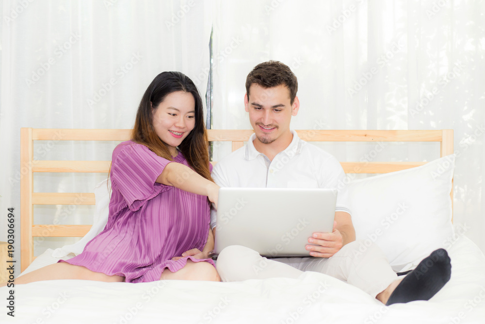 Beautiful pregnant family with laptop computer on bedroom, husband and wife notebook relax together, couple and family concept. Beautiful pregnant family with laptop computer on bedroom, husband and wife notebook relax together, couple and family concept.