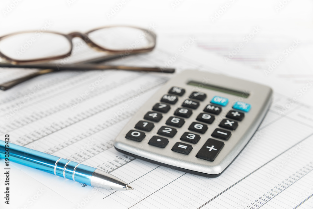 calculator, pen and glasses on a printed financial report with number tables, business concept for finance, economy and taxes calculator, pen and glasses on a printed financial report with number tables, business concept for finance, economy and taxes