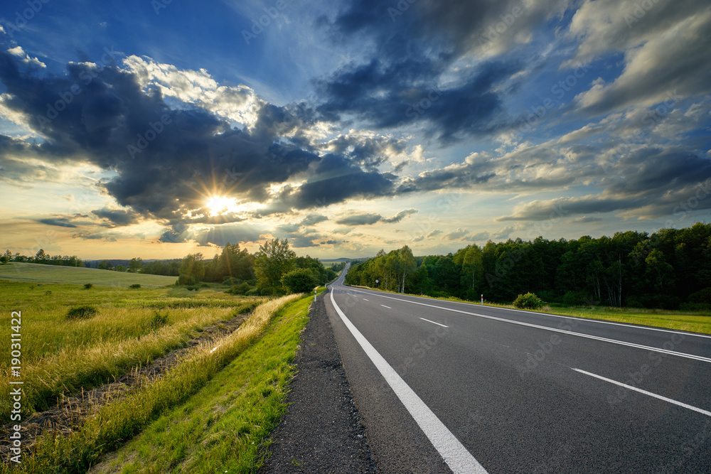 Empty asphalt road in the countryside at sunset with dramatic clouds Empty asphalt road in the countryside at sunset with dramatic clouds