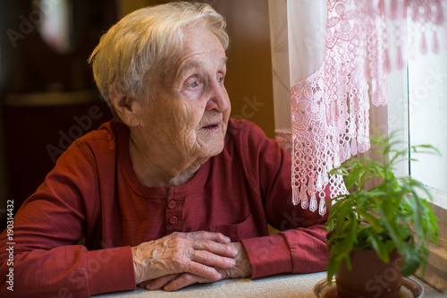 An elderly woman looks out the window.