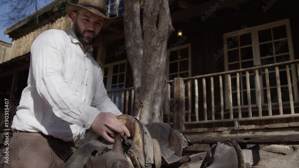 Cowboy man loading up saddle on wagon Cowboy man loading up saddle on wagon