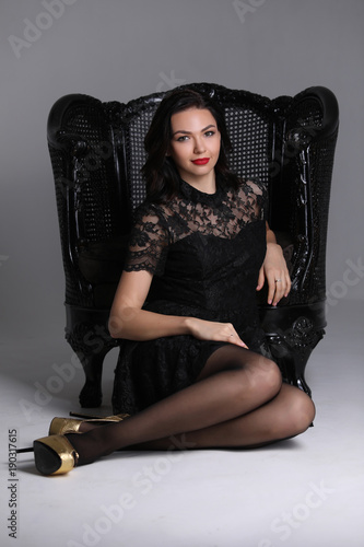 Woman in golden shoes sitting near the chair. Gray background. Photographie retouchee