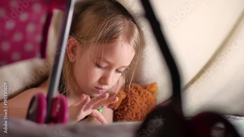 Cute little girl sitting on bed together with teddy bear playing games on tablet. photo