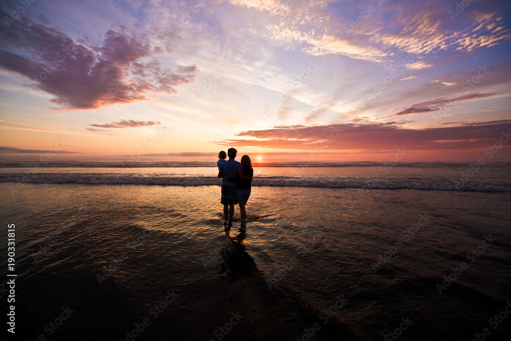 Silhouette of father and mother holding daughter on the beach at the sunset time. Outdoor and friendly family concept.Pacific Ocean, Sea Side Oregon USA, Family Vacation Time