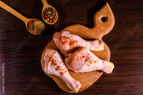 Chicken legs with the different spices on wooden cutting board. Top view