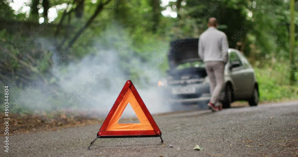 4K Stranded man with broken down car on a quiet country road, red warning triangle in foreground. Slow motion.