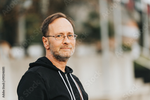 Outdoor portrait of 50 year old man wearing black hoody and eyeglasses