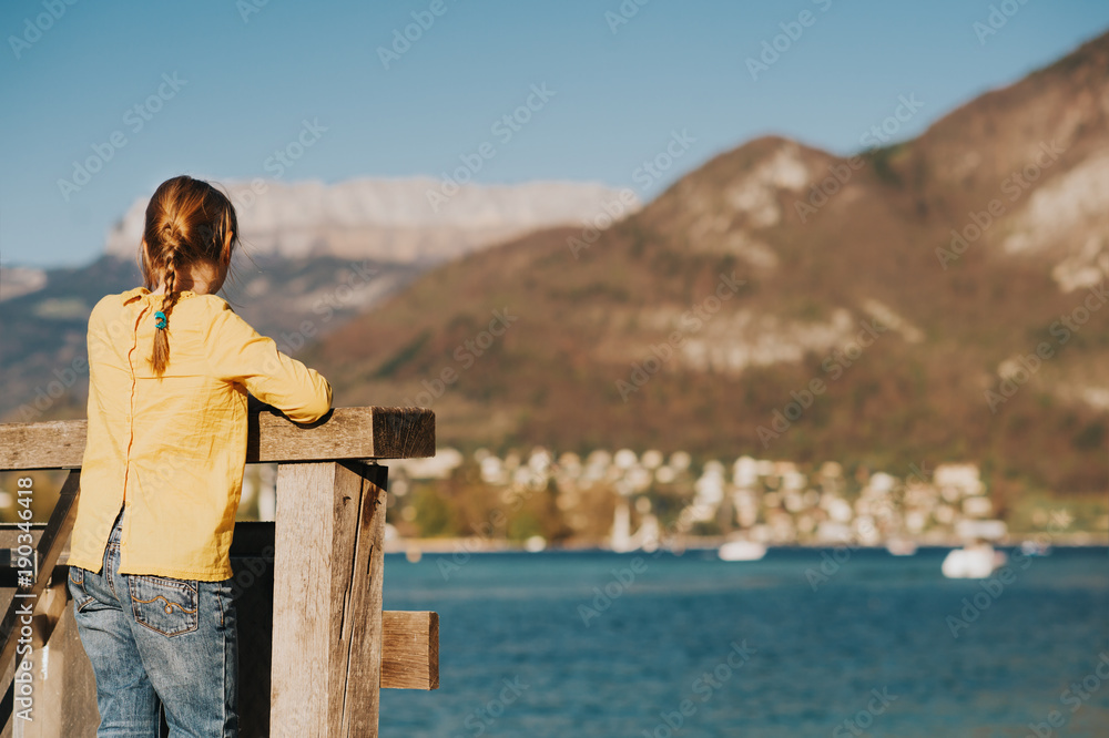 Little kid girl admaring Annecy lake in erly spring, family travel with children, back view Little kid girl admaring Annecy lake in erly spring, family travel with children, back view