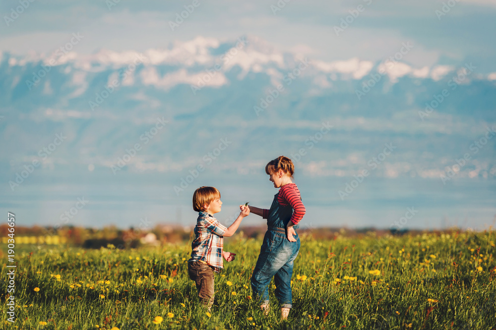Two kids, little brother and big sister, playing together outdoors in swiss fields with view on lake Geneva and french mountains Haute-Savoie. Image taken in Lausanne area, canton of Vaud, Switzerland