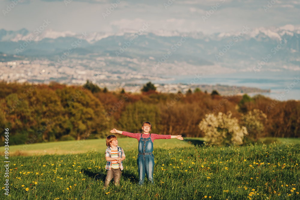 Two kids, little brother and big sister, playing together outdoors in swiss fields with view on lake Geneva and french mountains Haute-Savoie. Image taken in Lausanne area, canton of Vaud, Switzerland