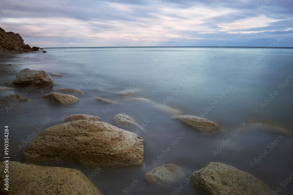 Evening by the sea, stones overgrown with moss in the water, and the sky at sunset. Long exposure, twilight.
