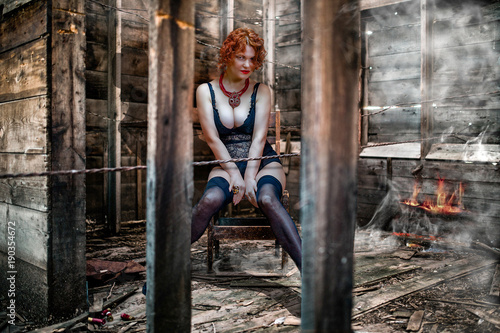 Beautiful, red-haired woman in negligee, in a dirty room on a chair