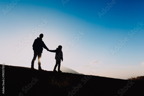 Silhouettes of father and son hiking at sunset