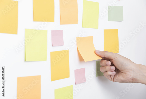 hand holding sticky note or post is on white bulletin billboard. business, teamwork, brainstorming concept