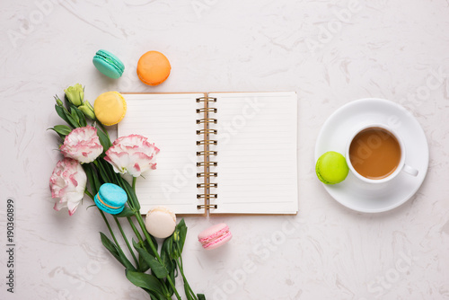 White desk with colorful macaroons, flowers, notebook, laptop and cup of coffee
