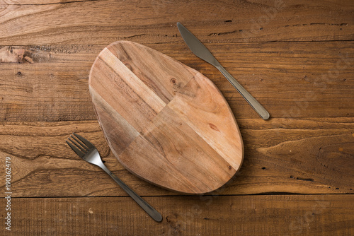 Oval cutting board with knife and fork on brown wooden background