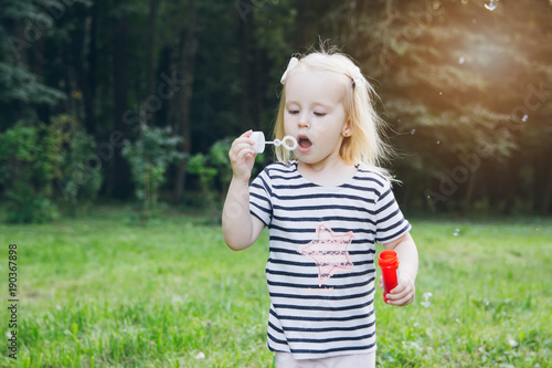 Little girl inflate soap bubbles on the lawn