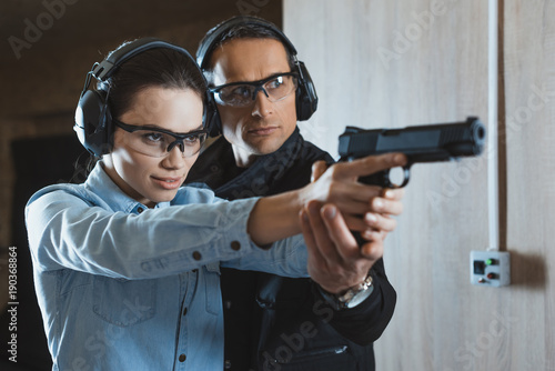 male instructor helping attractive female customer holding gun
