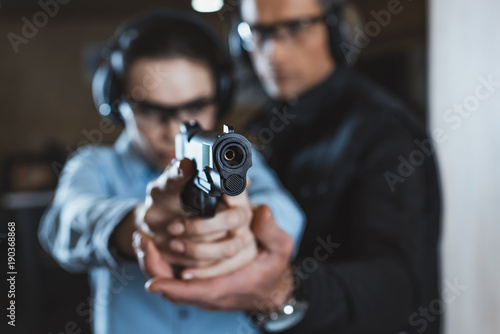 Instructor helping customer in shooting gallery with gun on foreground
