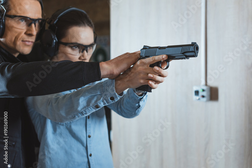 male instructor helping customer to shoot with gun in shooting range photo