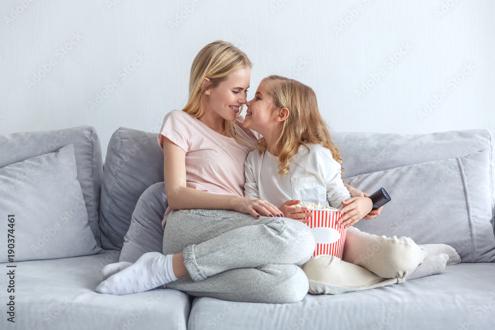 mother and daughter cuddling while sitting on couch at home