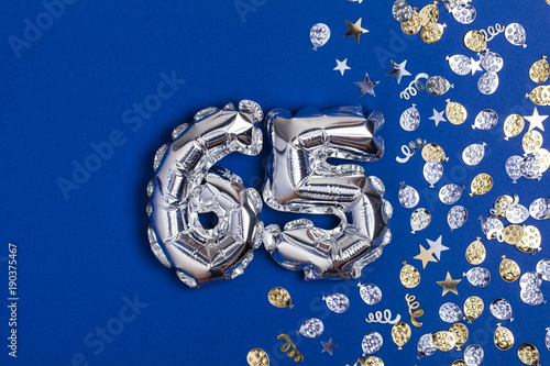 Silver foil number 65 balloon on a blue background with glitter gonfetti