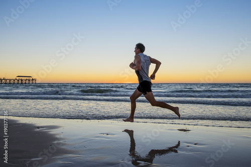 athletic fit and strong runner man training on Summer sunset beach in sea shore running and fitness workout in sport and healthy lifestyle