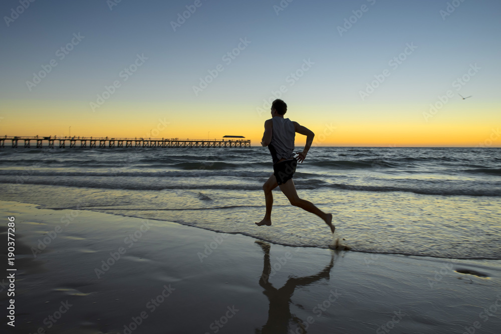 silhouette young dynamic athlete runner man with fit strong body training on Summer sunset beach running barefoot in sport healthy lifestyle concept