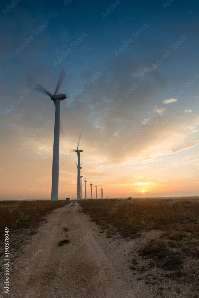 Obraz premium Wind turbines against red, blue and orange sunrise