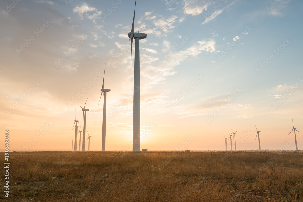 Fototapeta premium Wind turbines against red, blue and orange sunrise