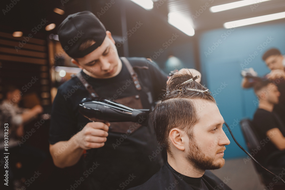 Barber shop. Barber dries hair of man with hair dryer and makes hair styling with hair dryer
