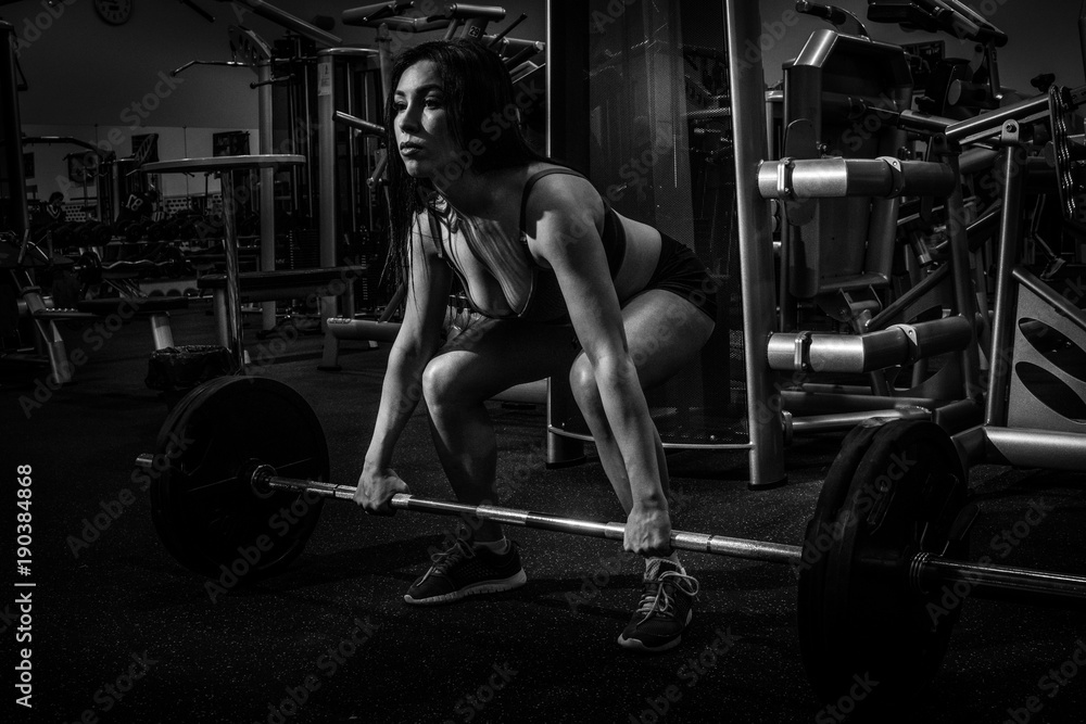 Portrait of a beautiful girl who crouches with a barbell in the gym. Sport life. bw Portrait of a beautiful girl who crouches with a barbell in the gym. Sport life. bw