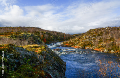 Beautiful autumn sunny landscape with a river between rocks. Bright autumn colors and trees without leaves against a blue sky with clouds © Ольга Страхова