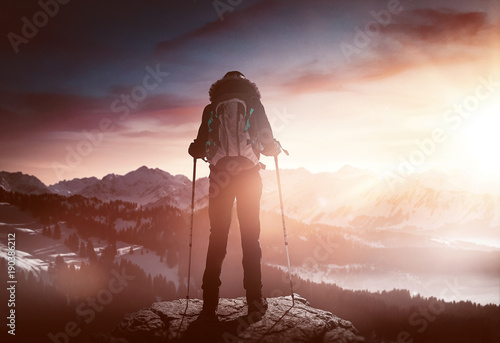 Bergsteiger steht auf Gipfel bei Sonnenaufgang