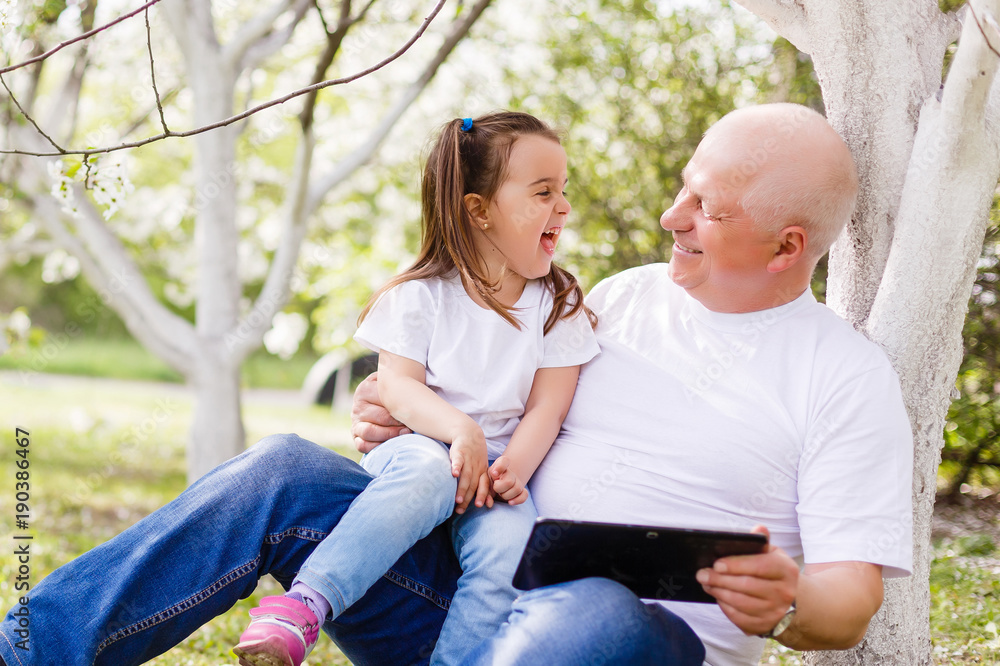 Happy grandfather with his granddaughter reading in a blooming garden