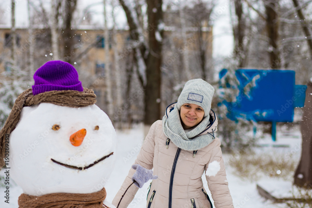 Stylish woman sculpt a big real snowman. Beautiful woman has fun in winter park, wintertime