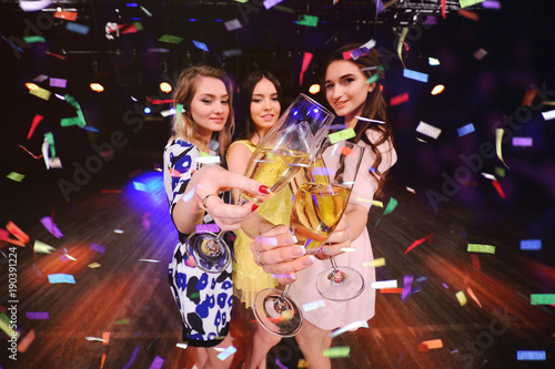 three pretty young girls with glasses of champagne having fun at a party in a nightclub.