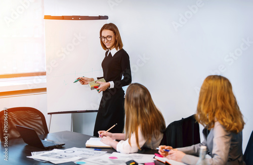 Smiling woman writing on large paper chart with marker in office and presents the diagram. photo