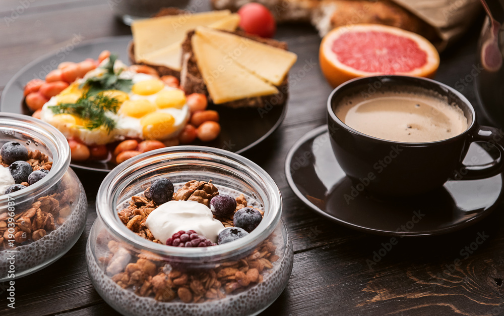 English breakfast. sausage, fried eggs and beans in tomato. coffee and bread nearby. chia with yogur and granola