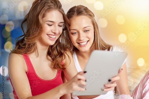 happy friends or teen girls with tablet pc at home
