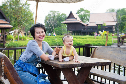 Mother looking at camera with her 10 months baby with vintage Thai house in background. © supong32