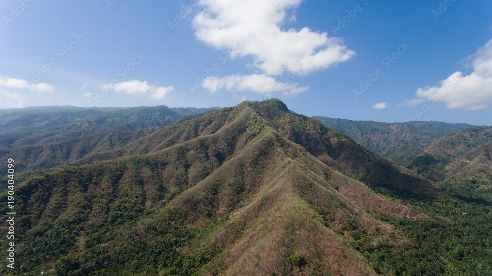 Fototapeta premium Aerial view of landscape, mountains covered with green forest, trees with sky and clouds, Bali,Indonesia. Slopes of the mountains are covered with forest in Asia. Travel concept.