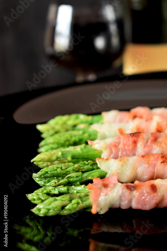 Green asparagus wrapped into smoked bacon on a black plate